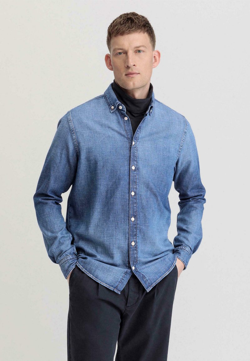 Lichtblauwe denim shirt met een button-down kraag, lange mouwen en een voorzak, gedragen over een zwarte turtleneck. Klassieke pasvorm.