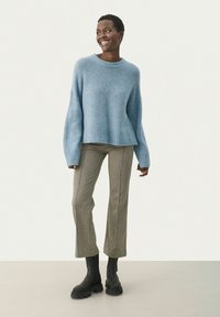 Un pull en maille oversized bleu clair avec un ourlet côtelé, associé à un pantalon écossais taille haute et des bottes noires à semelles épaisses.