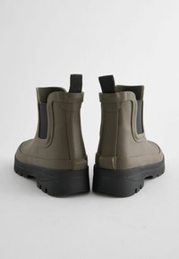 Bottes imperméables kaki avec un haut tige, des panneaux élastiques sur les côtés et une semelle en caoutchouc noir texturé, comportant des languettes pour un enfilage facile.