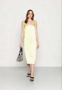 Vestido midi em cetim de cor verde claro, com alças finas, uma textura suave e uma silhueta ajustada. Combinado com uma bolsa de estampa de zebra e sandálias pretas.