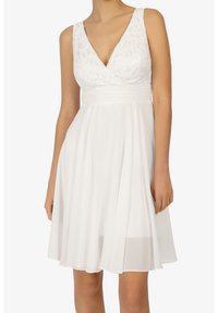 Robe blanche sans manches avec un corsage en dentelle texturée, décolleté en V profond et jupe évasée. Tissu lisse avec une taille froncée et un ourlet fluide.