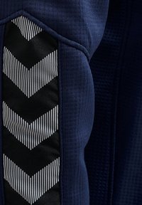 Tessuto atletico blu navy con superficie testurizzata, caratterizzato da un motivo a chevron rigato bianco e nero lungo il lato, che mette in risalto il contrasto e i dettagli.