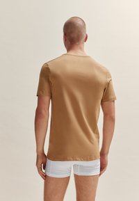 T-shirt à manches courtes, col rond en coton beige avec une texture lisse, présentant une coupe décontractée et sans embellissements visibles.