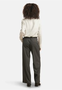 Light-colored, long-sleeve blouse paired with dark pinstriped trousers; details include a relaxed fit and pockets on the back of the pants.