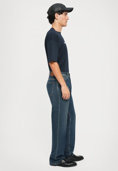 Marinblå oversized t-shirt, blå denimjeans med rak passform och svarta läderskor. Sidovy visar enkel design och texturer.