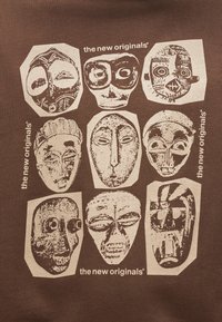 Neun stilisierte Stammesmasken mit markanten Gesichtszügen, angeordnet in drei Reihen auf braunem Hintergrund, mit der Beschriftung "die neuen Originale".