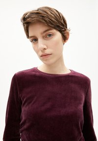 Burgunderfarbens Samtoberteil mit langen Ärmeln und rundem Ausschnitt, das eine weiche Textur und einen glatten Abschluss aufweist, geeignet für lässige Anlässe.