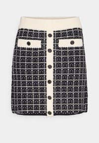 Černobílá tweedová sukně s pleteným pasem, předním zapínáním na knoflíky a dvěma náprsními kapsami s kontrastními akcenty a texturovaným vzorem.