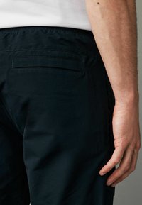 Sorte bukser med en baglomme, glat tekstur og afslappet pasform. Livremmen er elastisk for komfort.