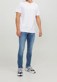 Camiseta blanca de manga corta, jeans de mezclilla azul claro en corte slim y zapatillas multicolores con detalles en blanco, marino y negro.