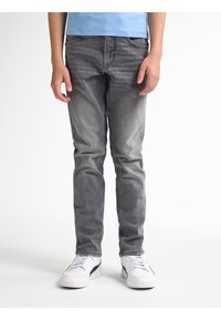 Vaqueros de denim gris con corte ajustado, presentando un leve desvanecimiento y arrugas, diseño de cinco bolsillos y combinados con zapatillas blancas.