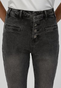 Jeans negros de cintura alta con cierre de botones, que cuentan con bolsillos delanteros y una textura deslavada, diseñados con un ligero elastano para mayor comodidad.