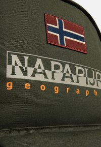 Zielony plecak z materiału z naszywką czerwonej flagi norweskiej i kontrastowym pomarańczowym napisem "NAPAPIJRI geography". Teksturowana powierzchnia.