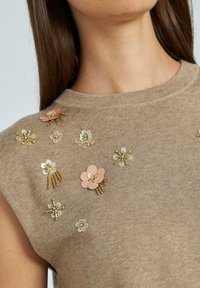 Suéter de punto beige con adornos florales en rosa y dorado, con lentejuelas y cuentas, creando una superficie texturizada.
