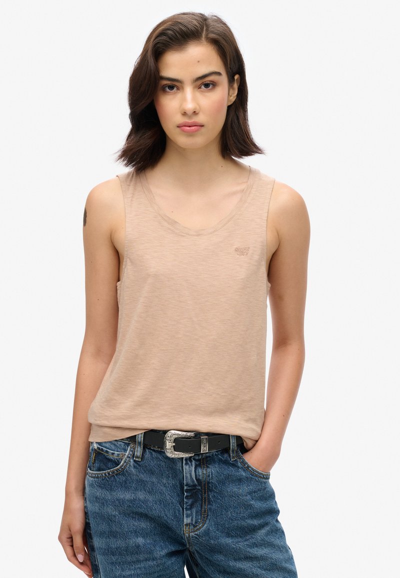 Top beige sin mangas con escote redondo, que presenta una sutil textura y un pequeño detalle de logo, combinado con unos jeans de mezclilla azul de tiro alto.
