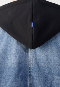Denim jacket with a black hood. Features light blue denim texture with contrasting black fabric, including a small blue brand tag.
