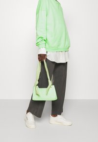 Ljusgrön strukturerad handväska med texturerad yta och knut-detalj på handtagen, i kombination med en överdimensionerad grön sweatshirt och lösa grå byxor.