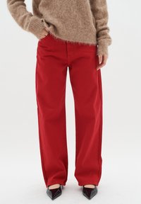 Pantalones anchos rojos de algodón resistente. Presentan una cintura alta, bolsillos laterales y un ajuste relajado, combinados con zapatos negros de puntera afilada.