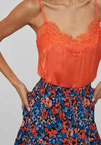 Orange silk camisole med spetsdetaljer i par med en utsvängd, svart blommig kjol som har röda, blå och rosa blommor i ett lagerdesign.