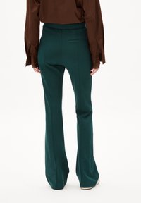 Pantalones acampanados verdes hechos de un material elástico, con una textura suave, un bolsillo trasero y una cinturilla ajustada.