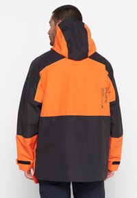 Waterproof jacket featuring a black body with bright orange accents, a hood, and reflective branding on the back. Loose fit with adjustable cuffs.