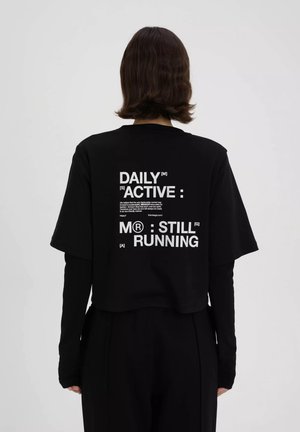Zwarte cropped t-shirt met bold wit tekst op de achterkant. Heeft korte mouwen en een relaxed fit, met meerdere tekstelementen en een logo.
