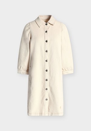 Rochie lungă crem cu nasturi, mâneci bufante, guler și buzunare laterale, prezentată pe un fundal deschis.