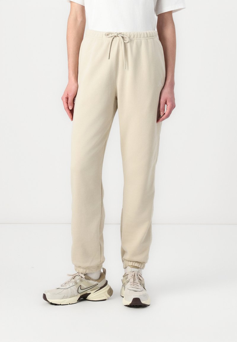 Beige joggebukser med elastiske mansjetter og snor i livet. Laget av mykt stoff, med en avslappet passform og glatt tekstur.