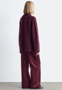 Übergroßer burgunderfarbener Pullover mit geripptem Saum, kombiniert mit weit geschnittenen Kordhosen in passender Farbe. Einfaches Design und weiche Textur.