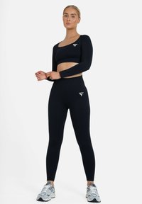 Black activewear set featuring a long-sleeve crop top and high-waisted leggings with ribbed texture and subtle logo accents.