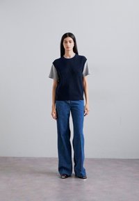 Marineblå genser i strikk over en grå t-skjorte, parret med blå vide jeans. Antrekket har et teksturert mønster og avslappet passform.