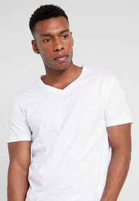 Hvid T-shirt med korte ærmer og V-hals, lavet af blød bomuld. Glat tekstur og afslappet pasform, velegnet til afslappet brug. Ingen bemærkelsesværdige mønstre eller accenter.