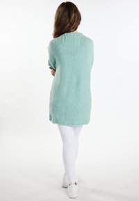 Långärmad, mintgrön stickad tröja med ribbat ok och lös passform, bärs över vita leggings. Texturen verkar mjuk och kraftig.