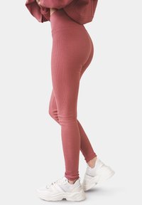 Ribbad vinröd leggings med hög midja, åtsittande silhuett och slät yta, i kombination med vita sneakers med grå detaljer.