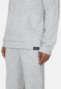 Set di felpa e pantaloni in pile grigio chiaro, tessuto testurizzato, con tasca frontale sulla felpa e patch del marchio sulla vita dei pantaloni.