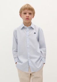 Camicia a maniche lunghe a righe in azzurro chiaro e bianco, con colletto button-down e un design ricamato di teschio navy sul lato sinistro del petto.