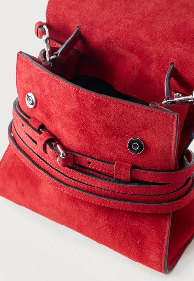 Τσάντα χειρός από κόκκινο σουέντ με άκρες σε μαύρη επένδυση, ασημένια κούμπωμα, και διπλό λουράκι κλεισίματος, απεικονισμένη ανοιχτή πάνω σε λευκό φόντο.