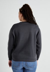 Grå hettegenser med rund hals, ribbestrikket kant og mansjetter. Kombinert med lyseblå jeans, sett fra baksiden med en jevn tekstur.