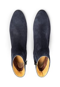 Botas de tobillo de ante en un azul marino oscuro con un acabado suave, con forro de cuero amarillo y cremalleras negras a los lados.