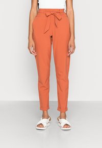 Calças ajustadas laranja com cinto de tecido, apresentando bainhas dobradas. Combinadas com sandálias brancas. Textura suave, design slim fit.