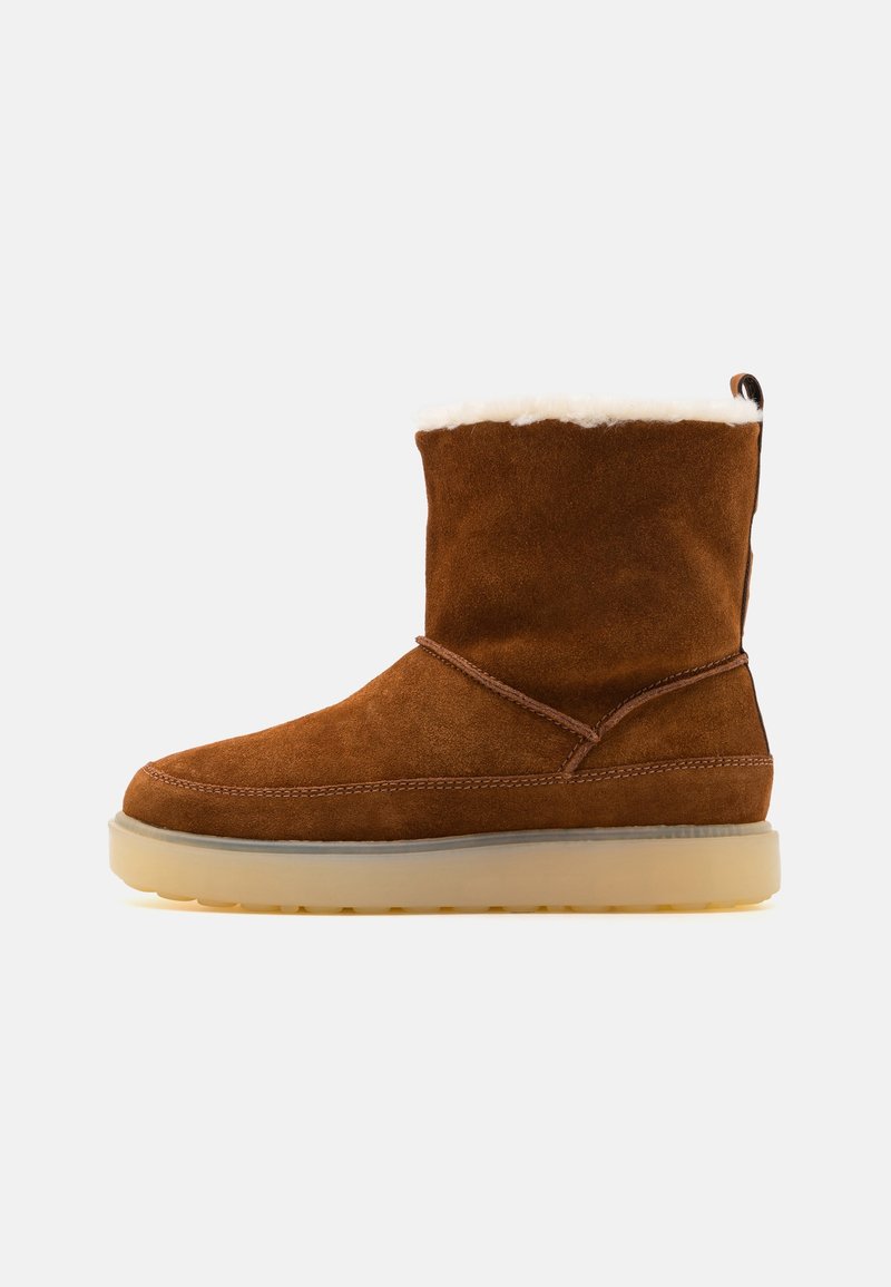 Botte d'hiver mi-mollet en daim brun avec doublure en polaire blanche, languette à l'arrière et semelle épaisse en caoutchouc de couleur claire.