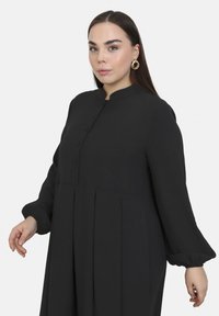 Schwarzes Hemdkleid mit langen, puffärmeligem Design und Plissee. Verfügt über einen runden Kragen und einen glatten, strukturierten Stoff.