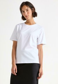 Hvid bomulds t-shirt med korte ærmer, rund halsudskæring og en afslappet pasform, parret med en sort nederdel. Enkelt og alsidigt design.