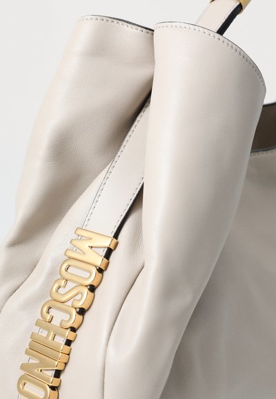 Beige leather bag with a sleek design, featuring a gold hardware accent with the brand name embossed prominently. Smooth texture, minimal stitching.
