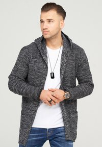 Gray knit cardigan with a hood, featuring textured yarn, two front pockets, and a relaxed fit, worn over a white shirt.