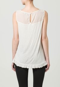 Witte mouwloze top met een transparante stippenpaneel en een keyhole-detail aan de achterkant. Kenmerkt zich door een rimpelrand en zachte, lichte stof.