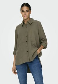 Camicia verde oliva con bottoni, colletto, maniche lunghe arrotolate ai polsini e vestibilità rilassata, realizzata in tessuto liscio con una sottile trama.