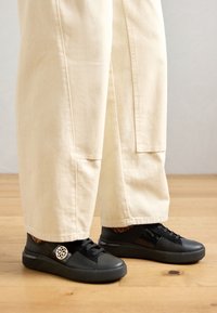 Baskets en cuir noir avec une surface texturée, une forme arrondie, un design à lacets et un accent de logo blanc distinctif sur le côté.