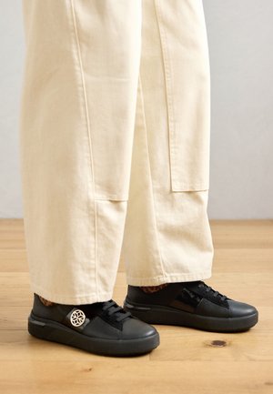 Black leather sneakers with a textured surface, rounded shape, lace-up design, and a distinctive white logo accent on the side.