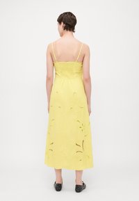 Vestido amarillo sin mangas con corsé ajustado y falda fluida, que presenta recortes florales y tirantes ajustables. Combinado con zapatos negros con tachuelas.